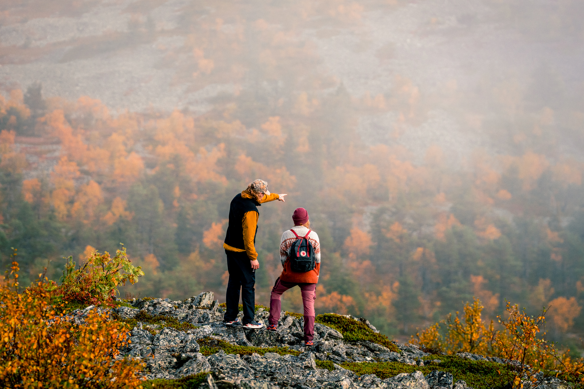 Mies ja nainen katsovat ruskan värien maalaamaan horisonttiin sumuisella tunturilla.