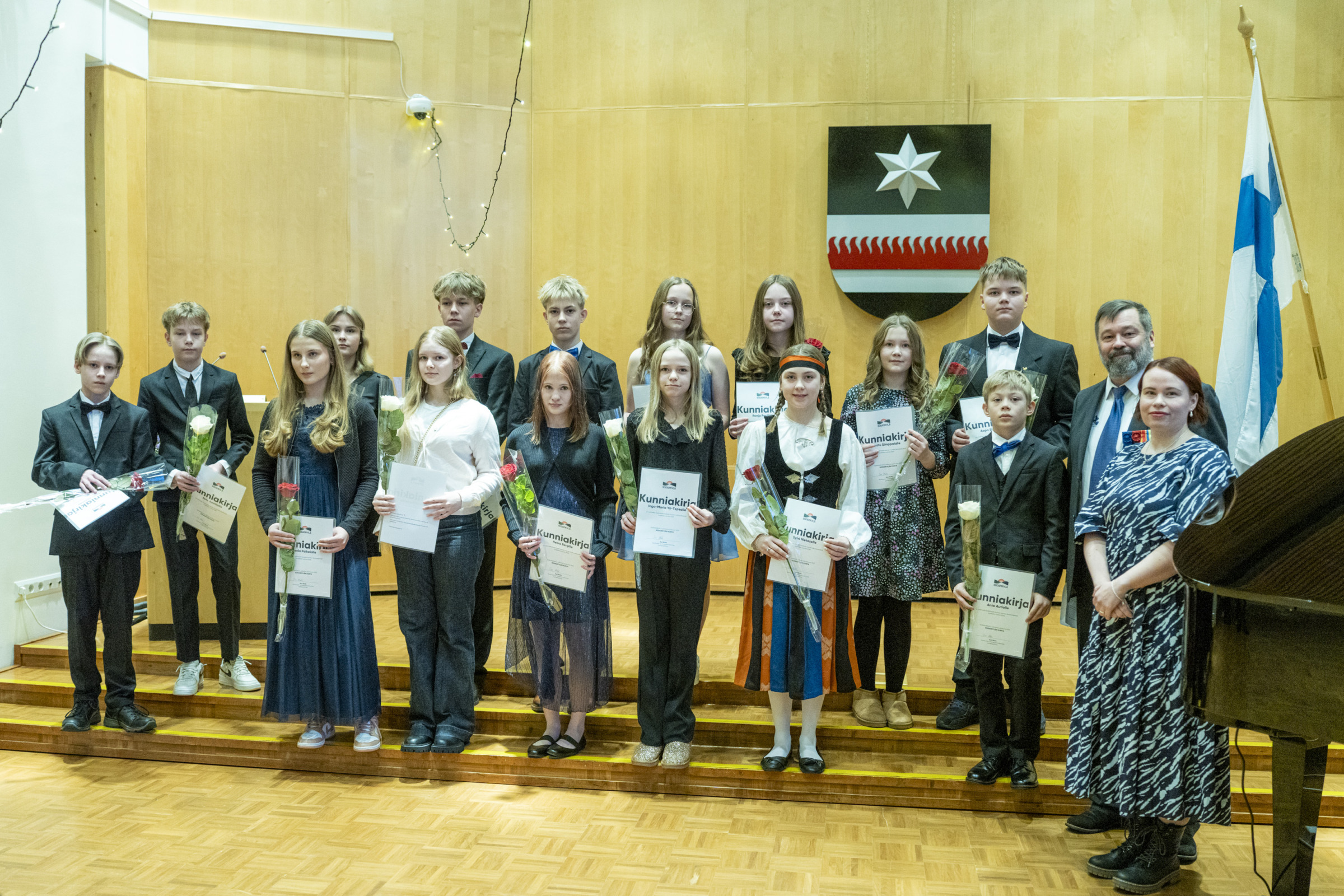 Nuoret kulttuuri- ja liikuntastipendillä palkitut kahdessa rivissä Sodankylän valtuustosalin portailla. Kaikilla on kunniakirjat ja ruusut käsissä. Kuvan oikeassa laidassa nuorten vieressä kunnanjohtaja Jari Rantapelkonen ja hyvinvointi- ja sivistyslautakunnan puheenjohtaja Suvi Ahola.